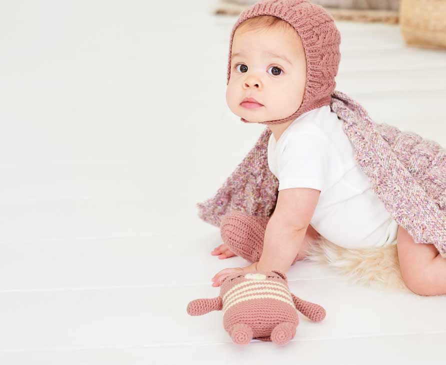 Baby mit Strickmütze, gestrickter Babydecke und gehäkeltem Kuscheltier