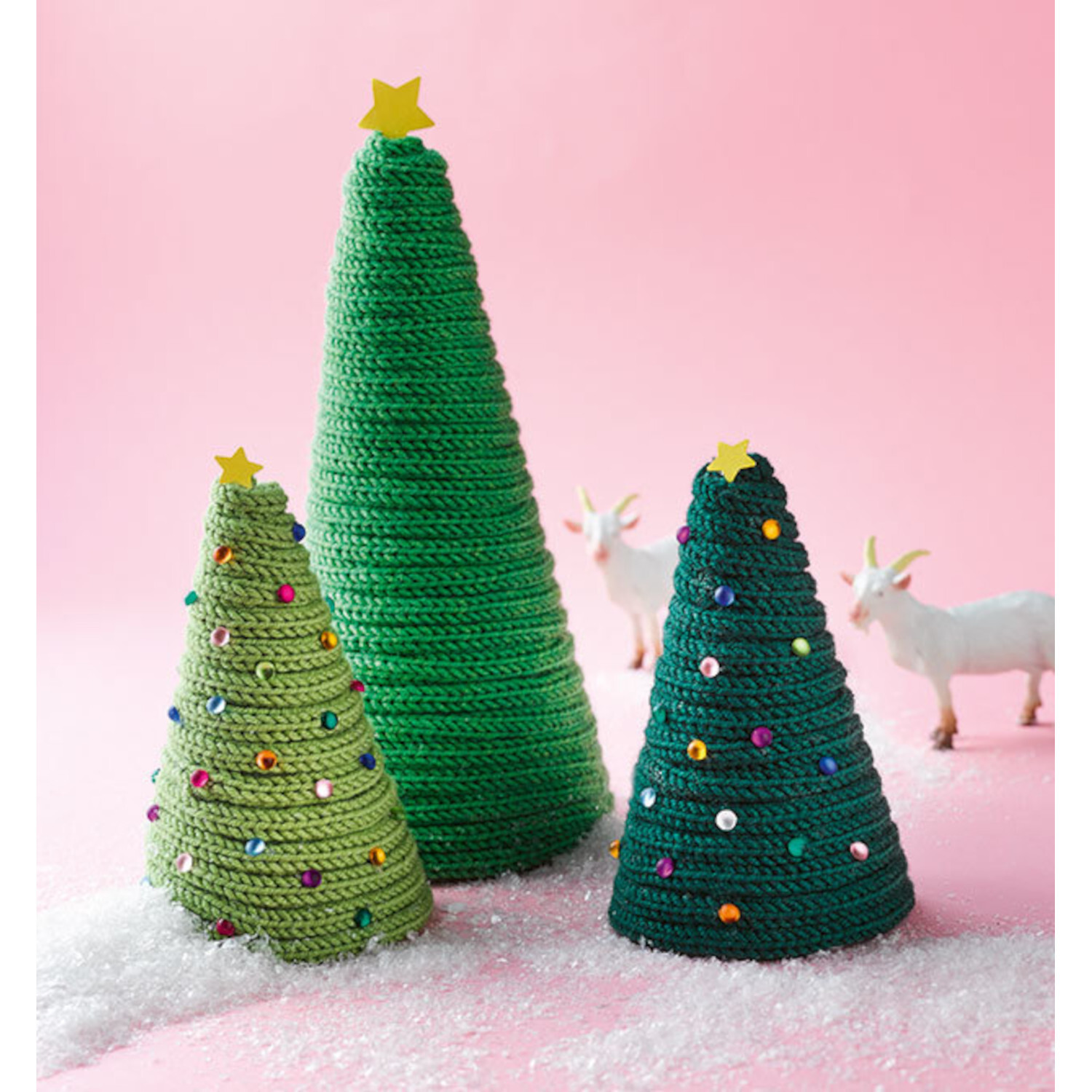 Kreativ kinderleicht Strickliesel: Drei gestrickte Tannenbäume in Grün mit bunten Perlen auf rosa Hintergrund.