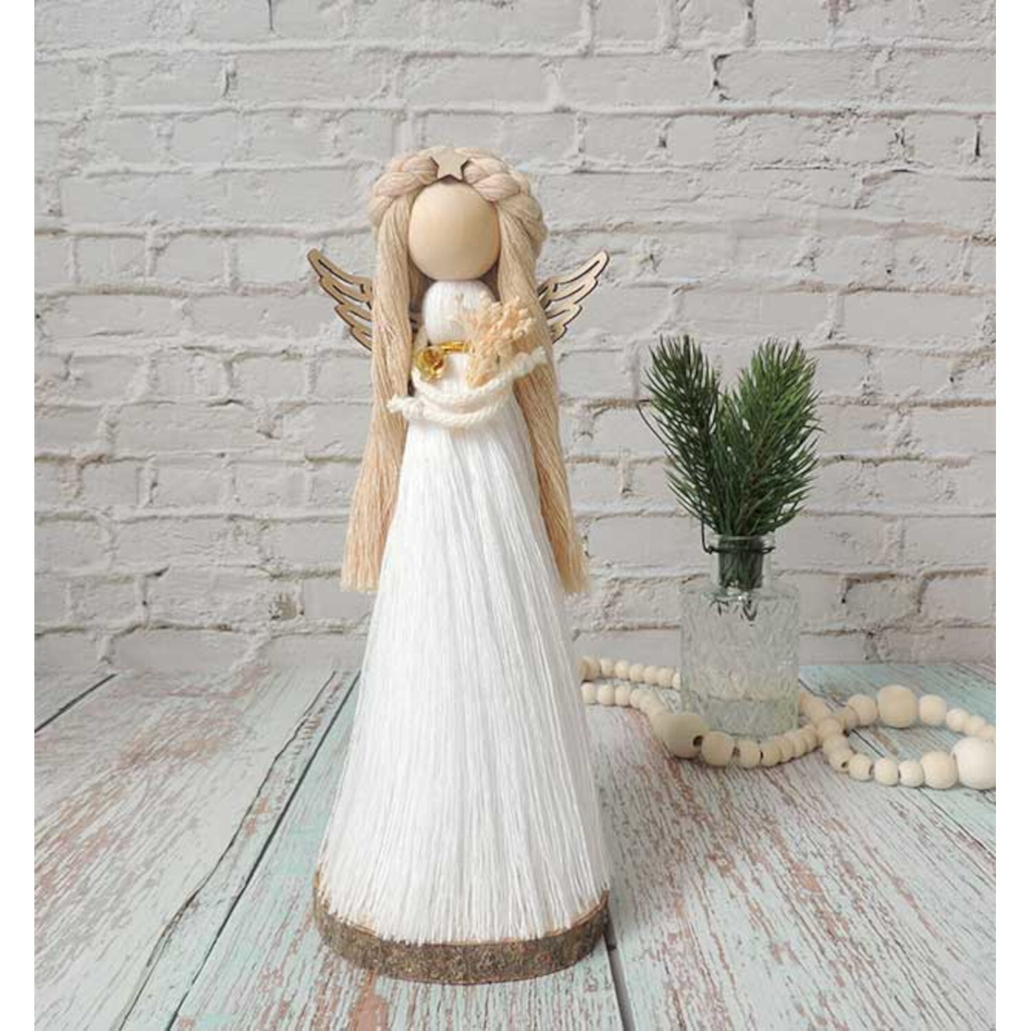 Märchenhafte Makramee Engel: Handgefertigte Figur in Weiß mit goldenen Flügeln vor Ziegelwand.