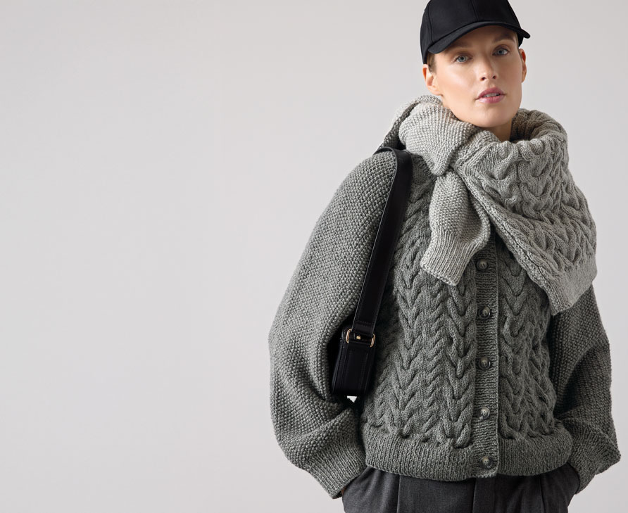 Frau trägt dunkelgrauen Strickpulli und hellgrauenStrickpulli um die Schultern gebunden.